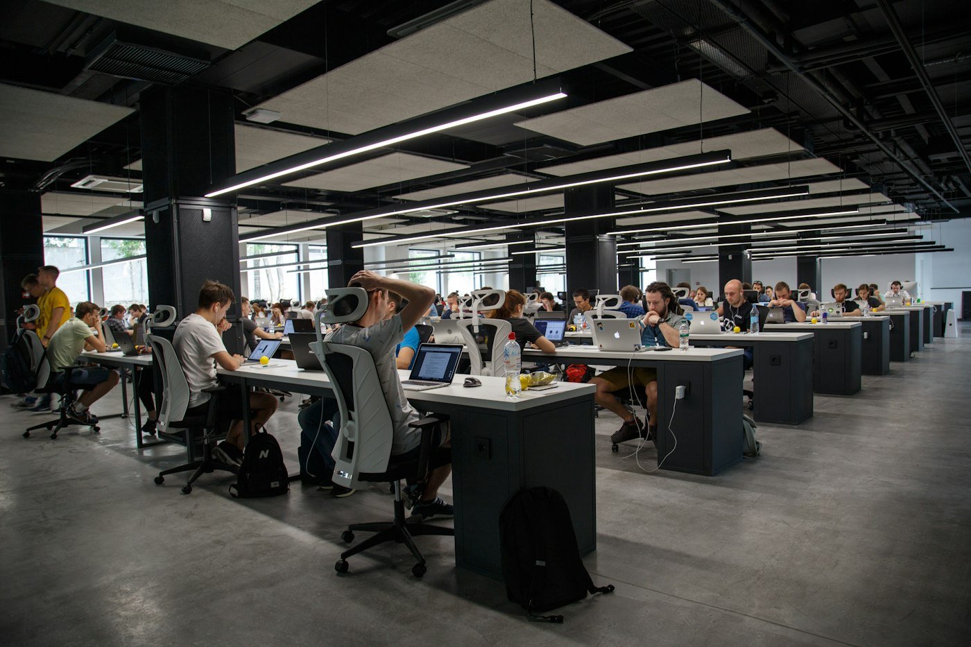A large open office with rows of desks, laptops, and people working at screens